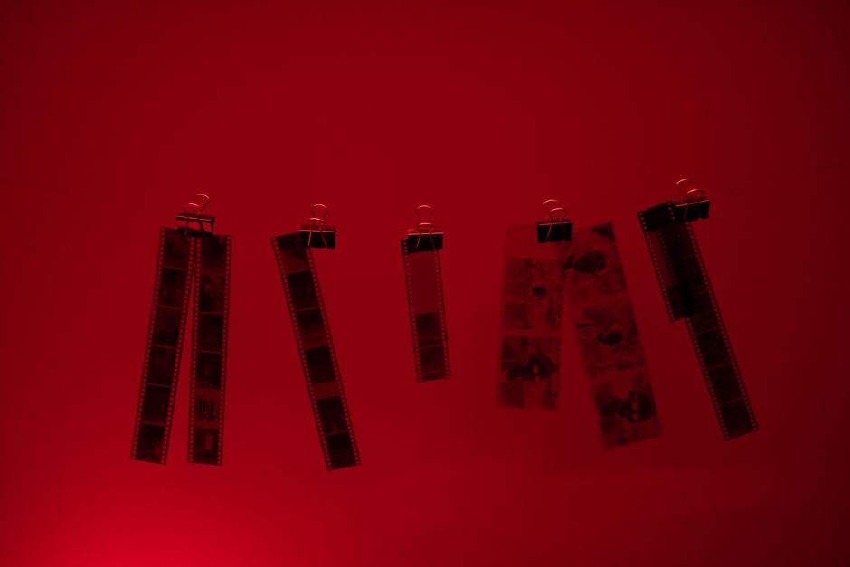 Hanging film strips illuminated by red darkroom light during development.