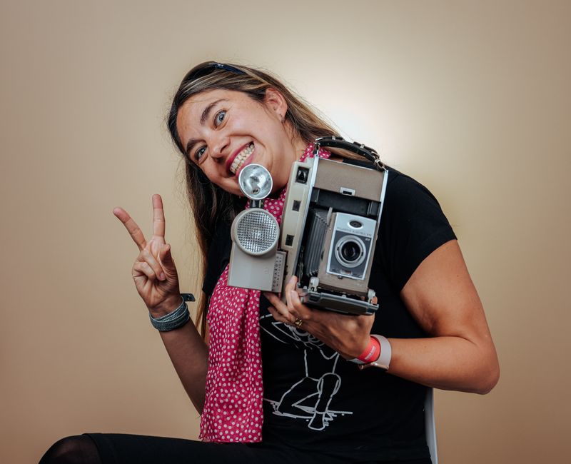 Happy woman holding vintage camera with a peace sign, capturing a nostalgic vibe.
