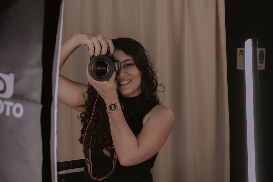 A smiling woman holding a camera in a photography studio setting.