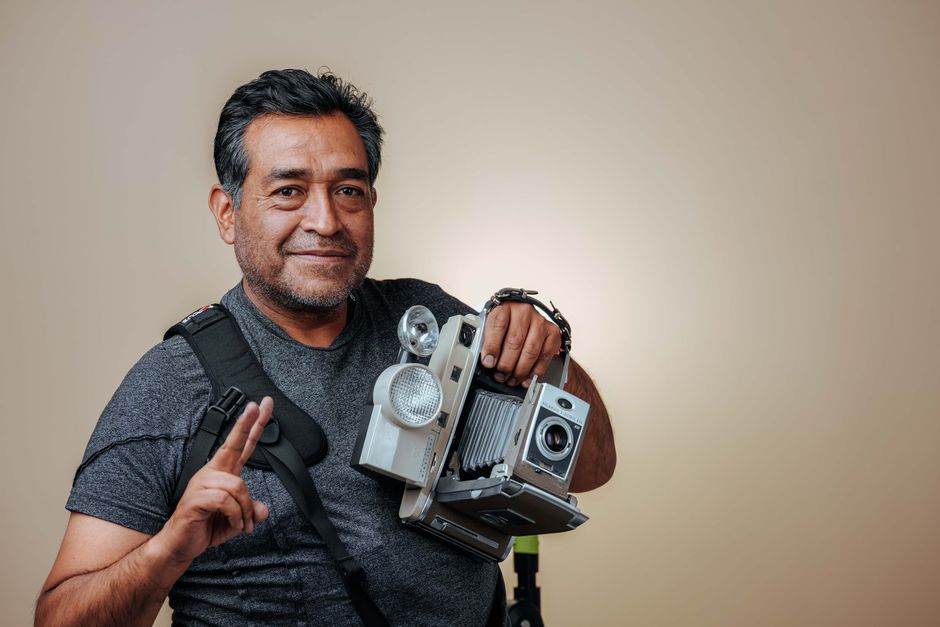 Smiling adult man posing with vintage camera in a studio setting.