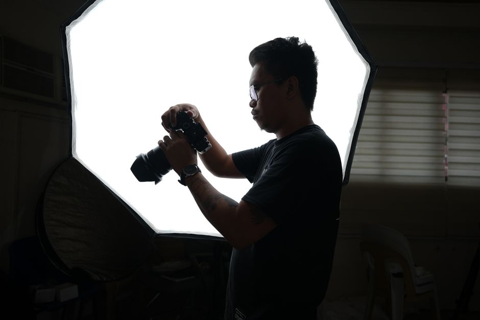 A professional photographer adjusting camera equipment in a studio setting with softbox lighting.